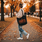 Woman walking through fall leaves with an iced coffee and a black FARTS tote bag that says "Find A Reason To Smile" in bold orange letters, spreading gratitude and mental wellness through fashion